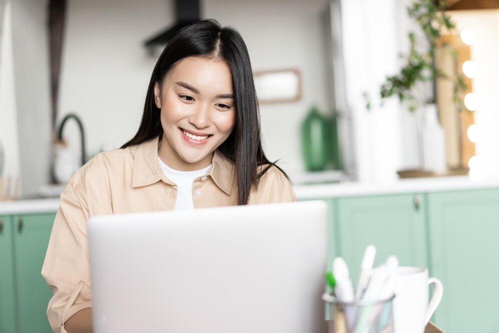 smiling-asian-girl-using-laptop-working-from-home-computer-pc-sitting-kitchen-studying-doi_1258-84404