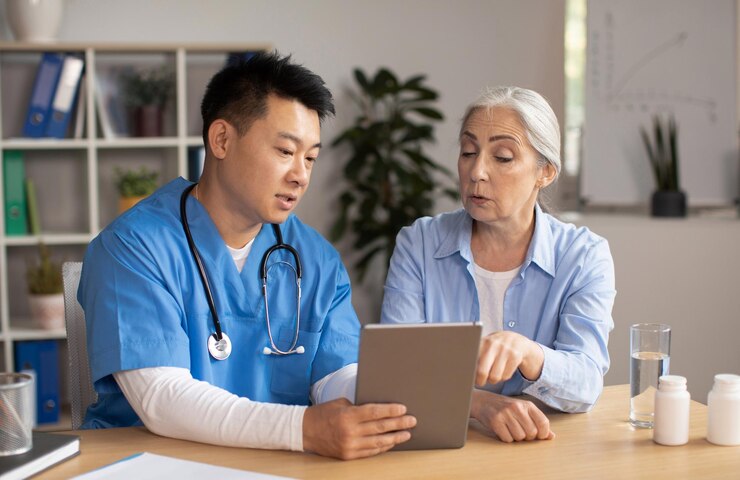 serious-middle-aged-korean-male-doctor-showing-tablet-consulting-senior-european-lady-patient-clinic_116547-43961